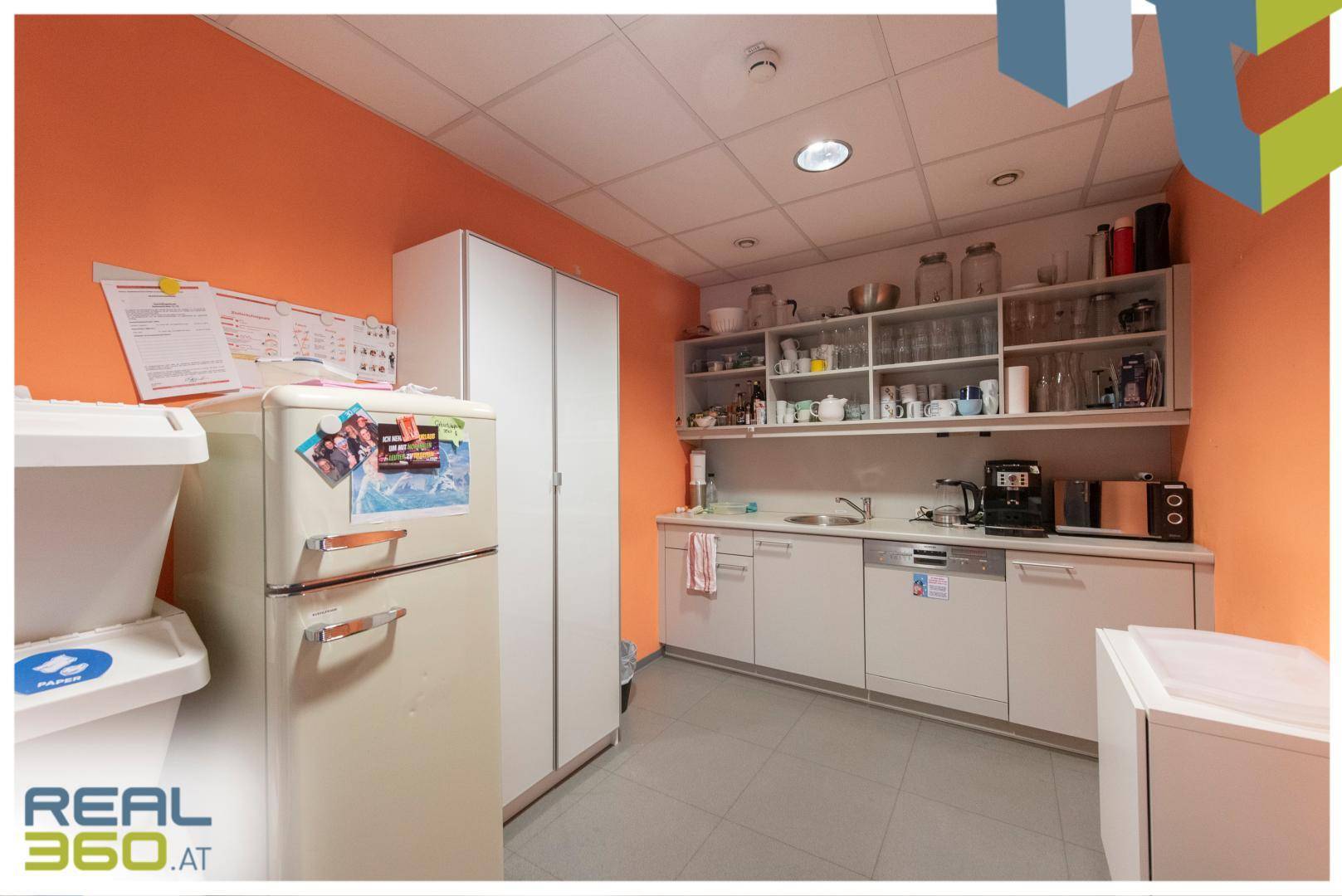 Funktionale Büroküche mit Kühlschrank, Spüle und offenen Regalen, ideal für Mitarbeiterpausen.