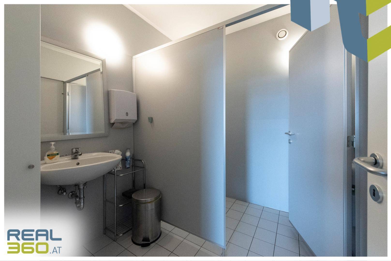 Saubere Toilettenanlage mit Waschbecken, Spiegel und mehreren Kabinen, funktional und gut gepflegt.