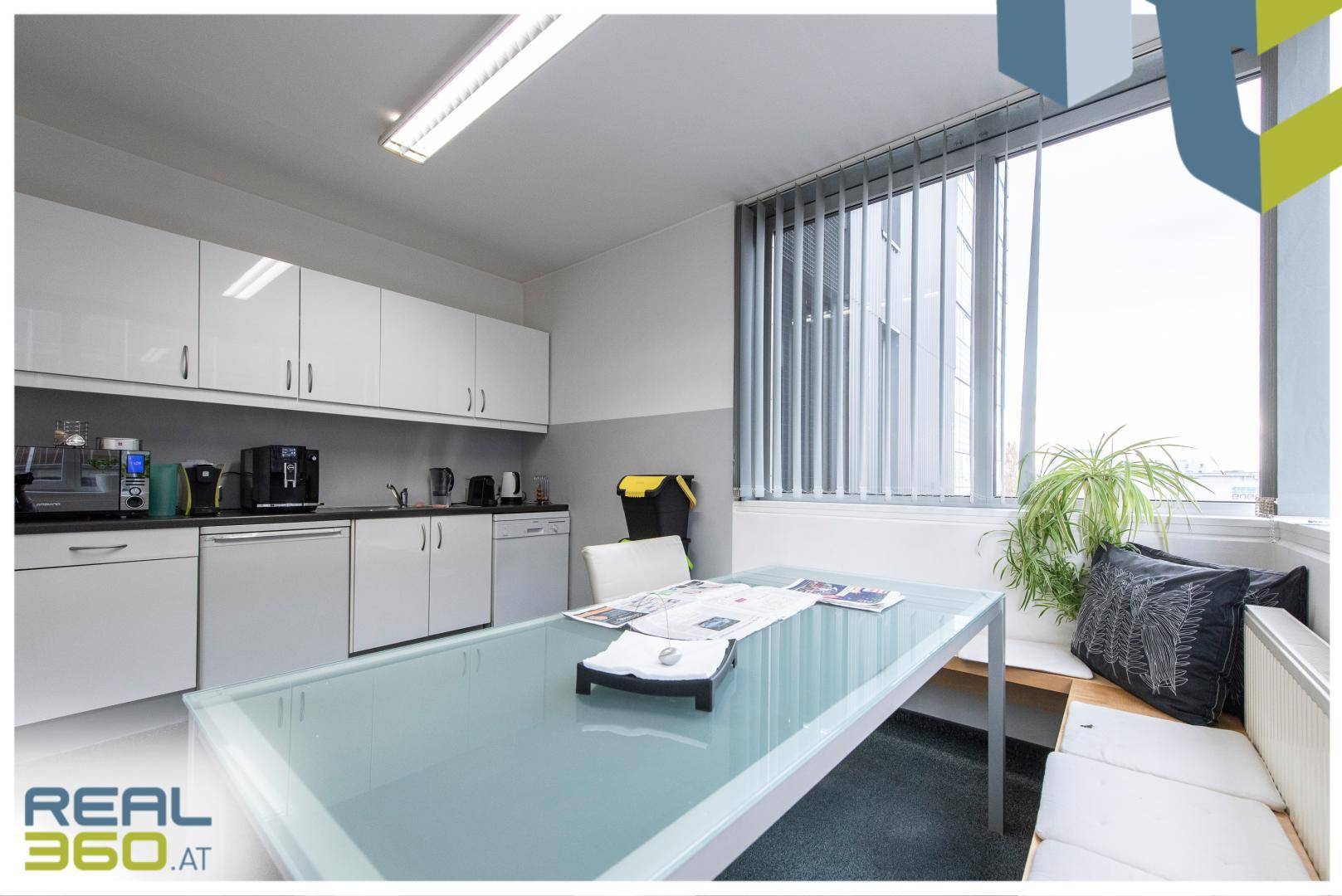 Moderne Teeküche mit weißen Hochglanzschränken, Spülmaschine und einem großen Tisch mit Sitzbank, sehr funktional.