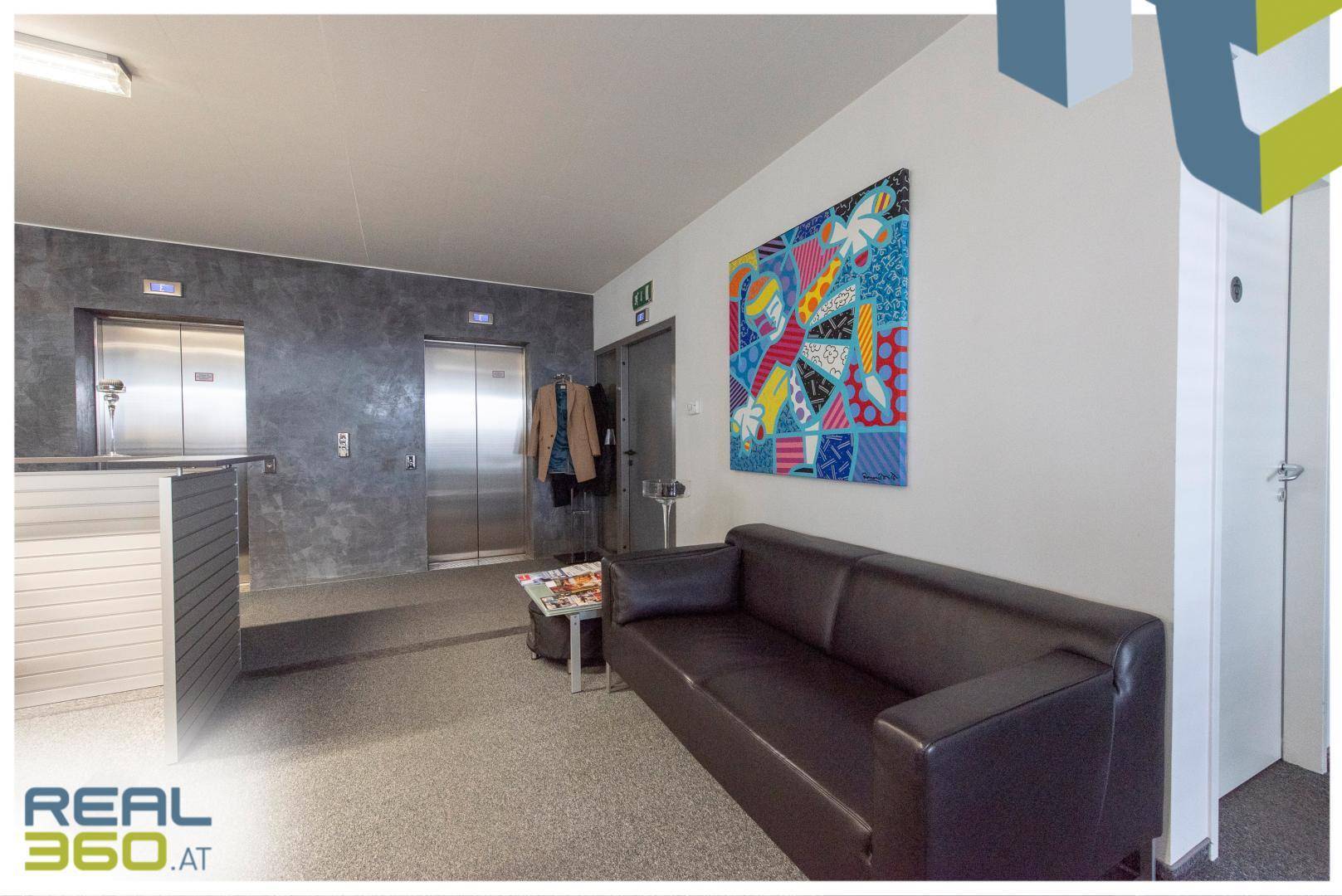 Wartebereich mit bequemer Couch, Kunstwerk an der Wand und Aufzügen im Hintergrund, einladend und modern gestaltet.