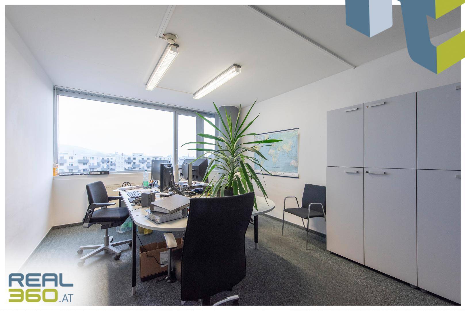 Geräumiges Büro mit mehreren Arbeitsplätzen, großen Fenstern und einem Weltkarten-Wandbild, hell und funktional.