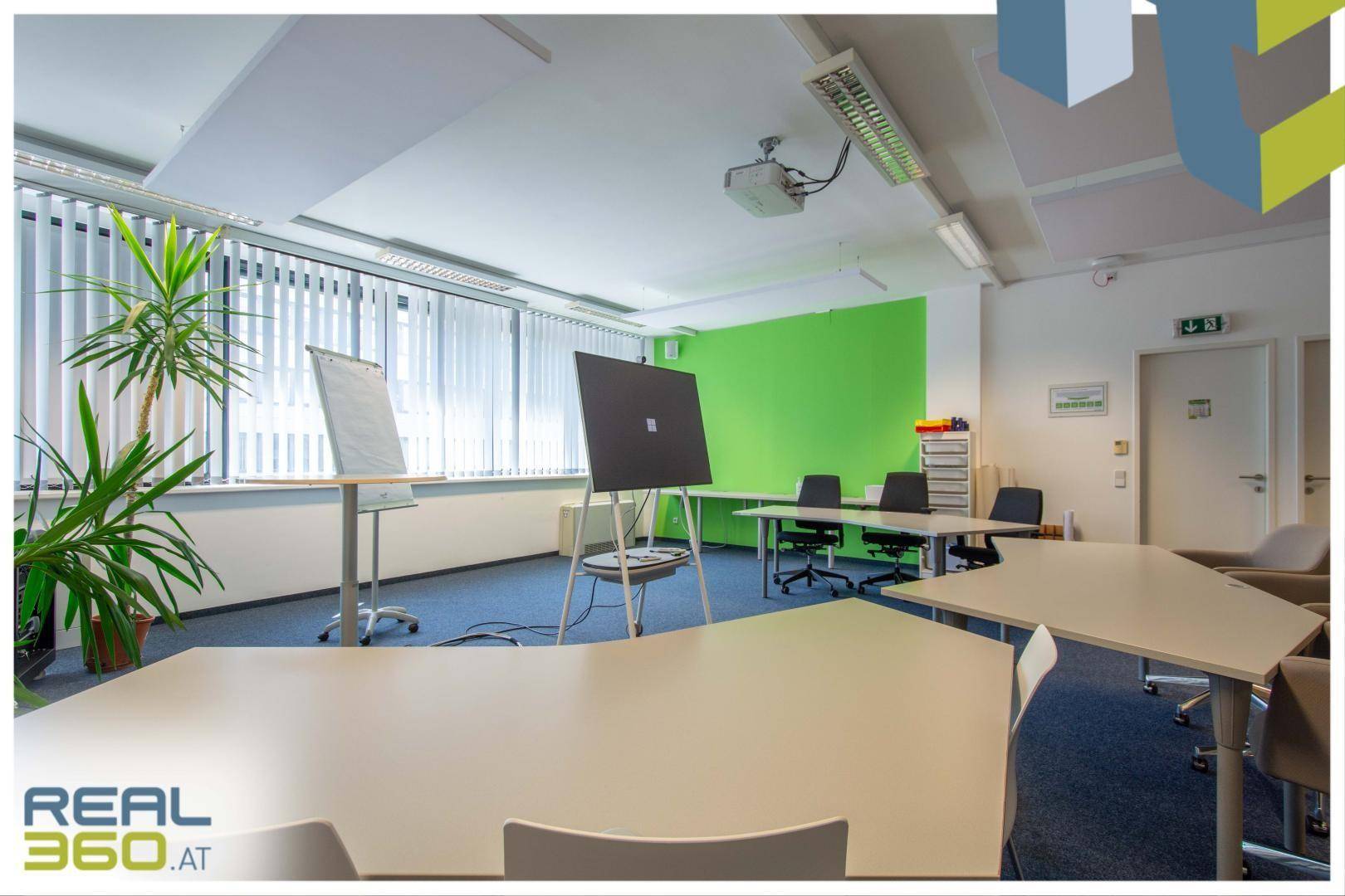 Heller Konferenzraum mit Projektor, Whiteboard und grüner Akzentwand, ideal für Besprechungen.