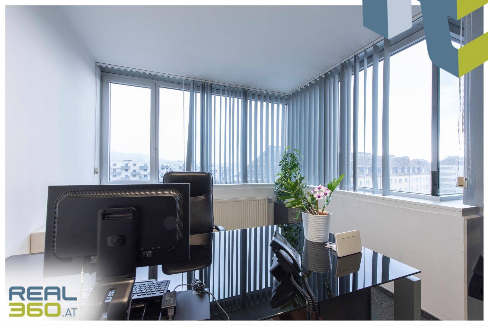 Einzelner Arbeitsplatz in einem hellen Büro mit großem Fenster und Blick auf die Stadt.