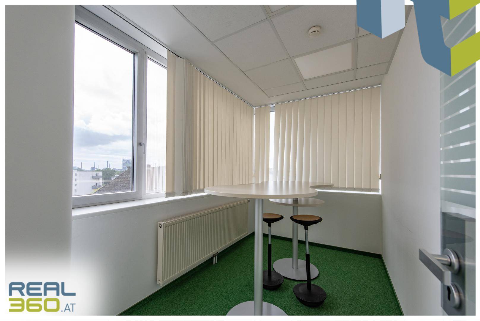 Kleiner Stehtischbereich mit Hockern und Fenstern, ideal für kurze Pausen oder informelle Treffen.