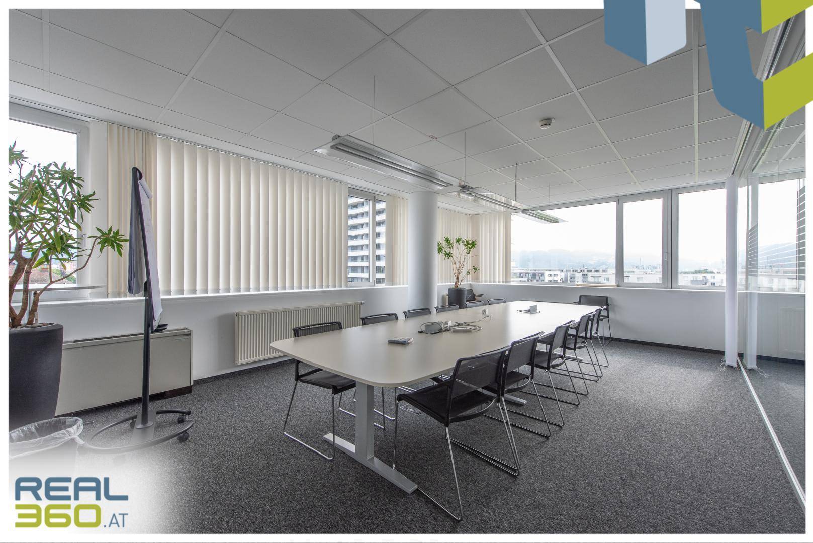 Heller Konferenzraum mit großem Tisch, vielen Stühlen und weitem Ausblick durch die Fenster.