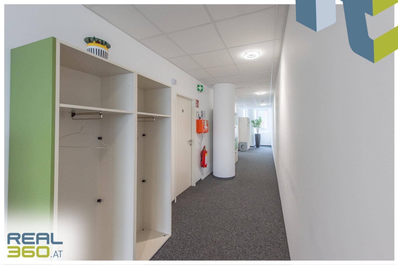 Langer Büroflur mit Teppichboden, Garderobenschränken und Brandschutzvorrichtungen.