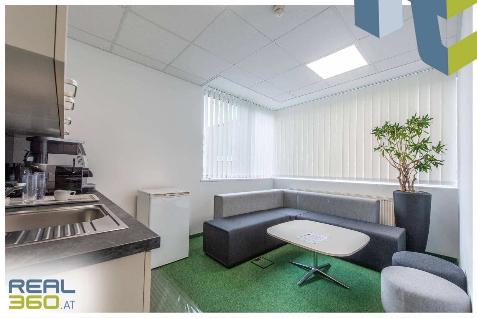 Gemütlicher Pausenraum mit kleiner Küchenzeile, Sofa und Blick nach draußen durch das Fenster.