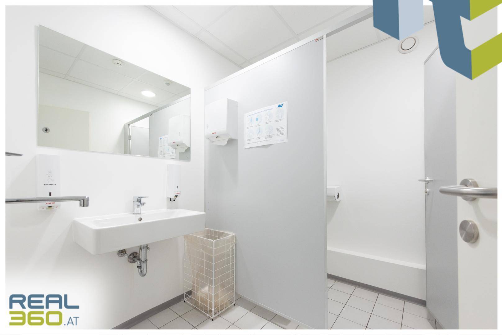 Heller und sauberer Toilettenraum mit modernem Waschbecken, großem Spiegel und weißen Fliesen.