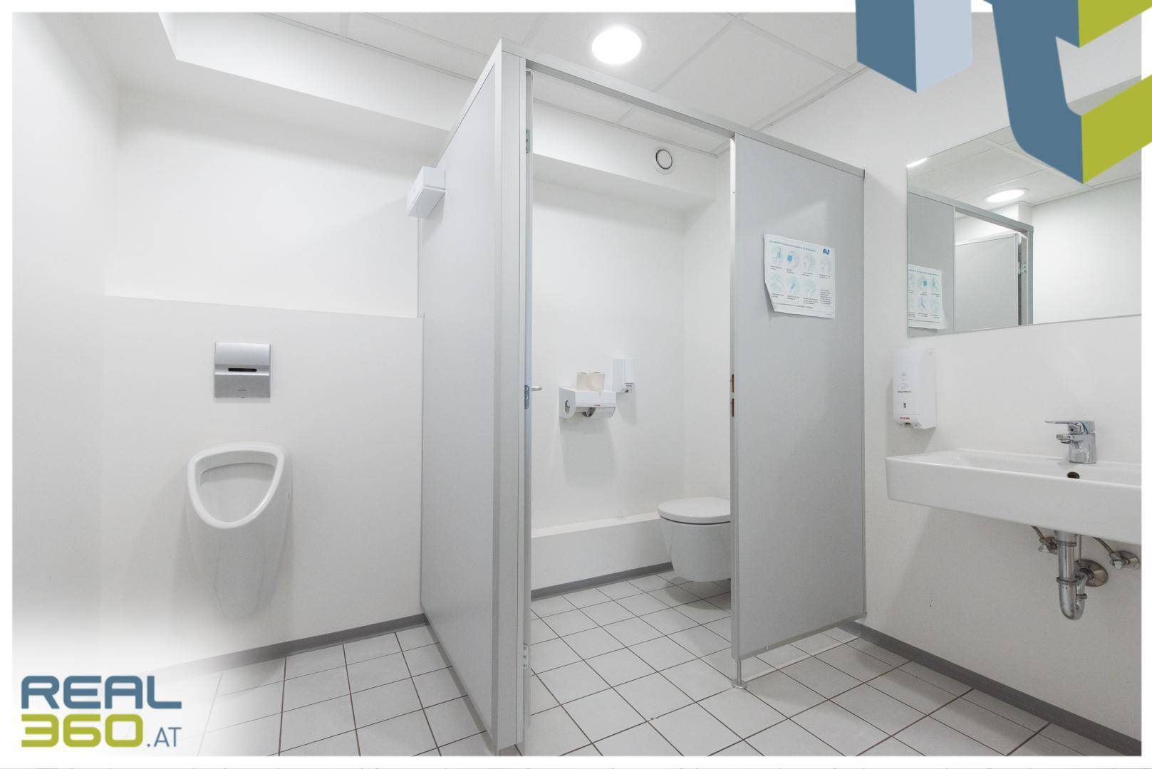 Heller und sauberer Sanitärbereich mit mehreren Toilettenkabinen, Urinal und Waschbecken.