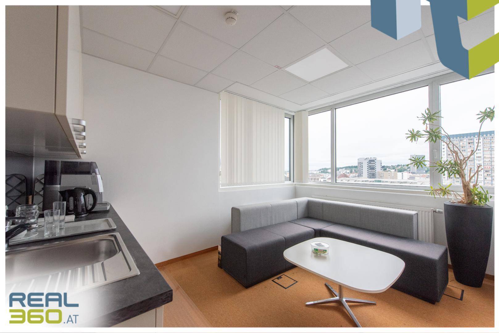 Kleine Teeküche kombiniert mit einem Loungebereich, Sofa und Fenster mit Stadtblick.