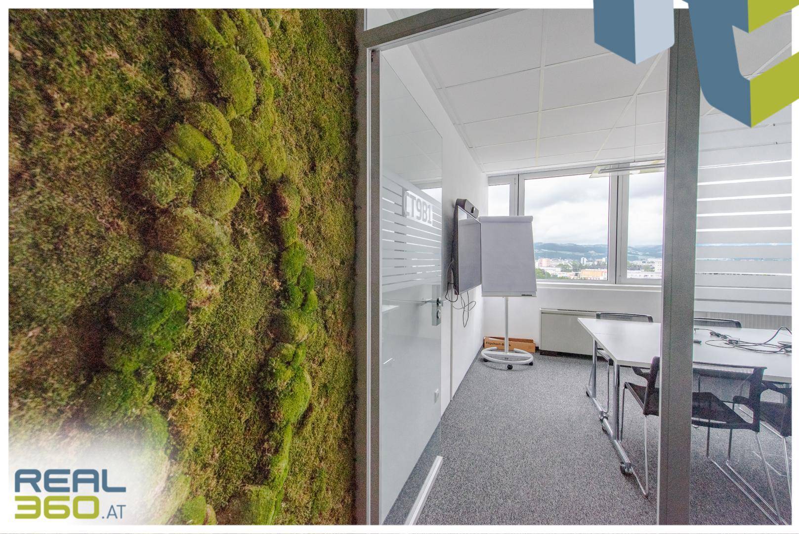 Konferenzraum mit Mooswand, Glastür und Whiteboard, bietet einen hellen Arbeitsbereich.