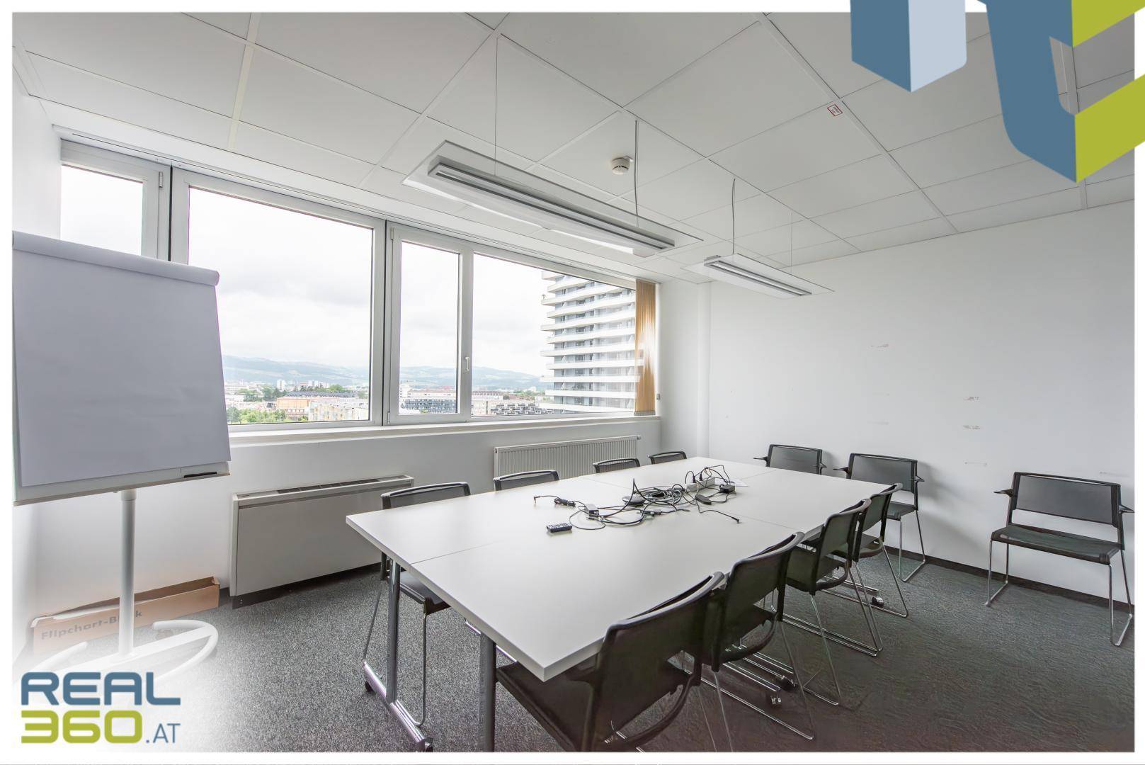 Heller Konferenzraum mit großem Tisch, vielen Stühlen und weitem Blick über die Stadt und Berge.