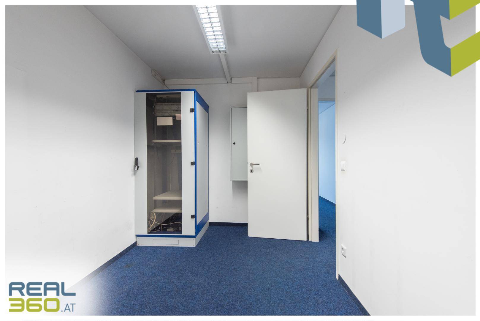 Kleiner Büroraum mit blauem Teppichboden, weißen Wänden und einem Serverschrank.