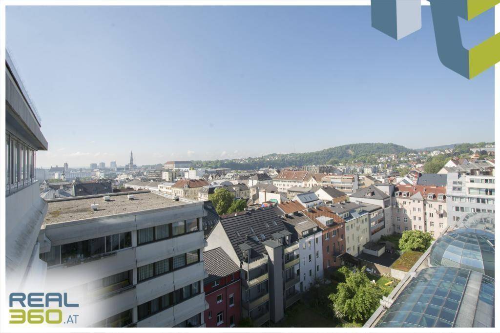 Panoramablick über die städtische Bebauung und die umliegenden grünen Hügel an einem klaren Tag.