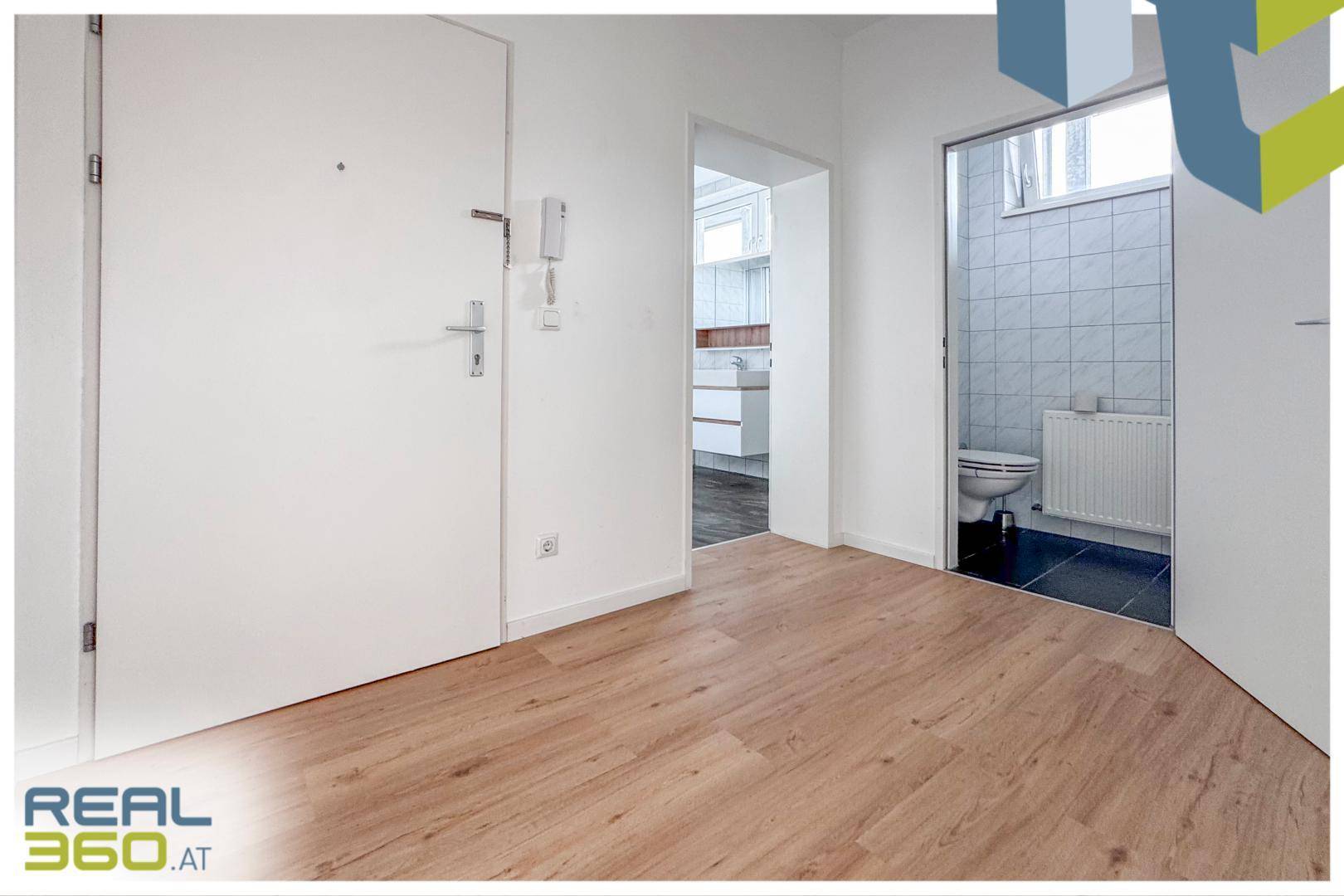 Heller Eingangsbereich mit Laminatboden und Zugang zu einem gefliesten Badezimmer.
