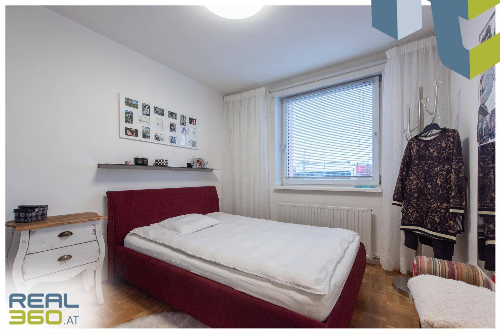 Gemütliches Schlafzimmer mit rotem Bett, Parkettboden und Fenster für natürliches Licht.