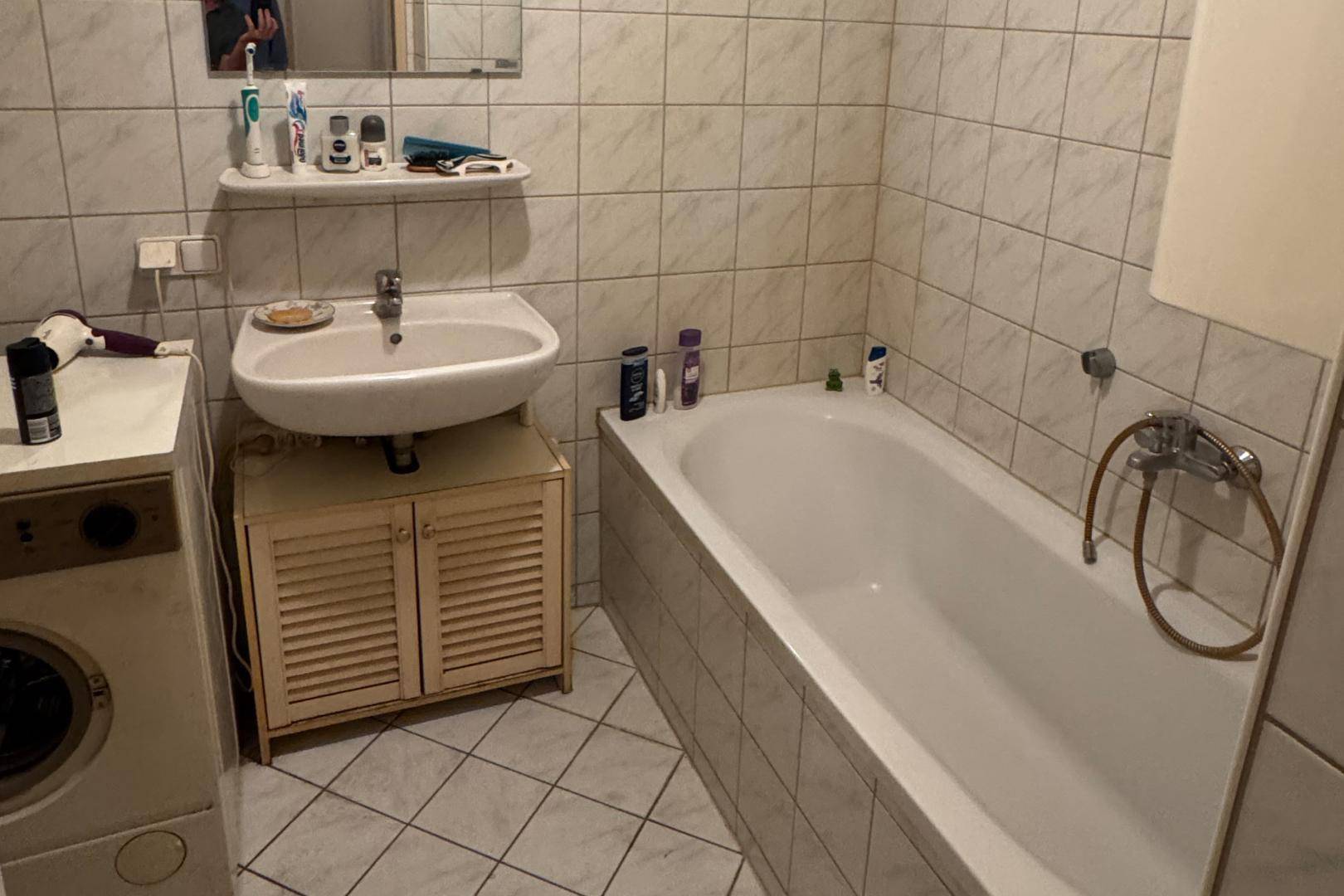 Funktionales Badezimmer mit Badewanne, Waschbecken und Waschmaschine, hell gefliest.