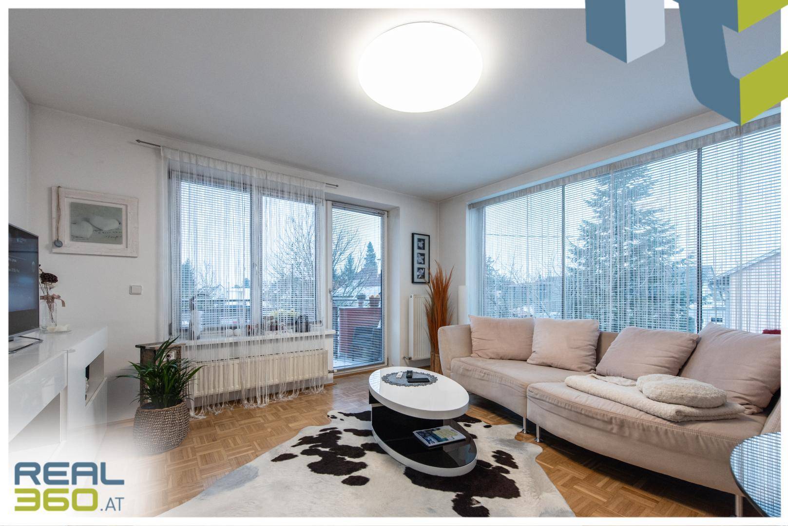 Helles Wohnzimmer mit bequemer Couch, Parkettboden und Zugang zum Balkon.