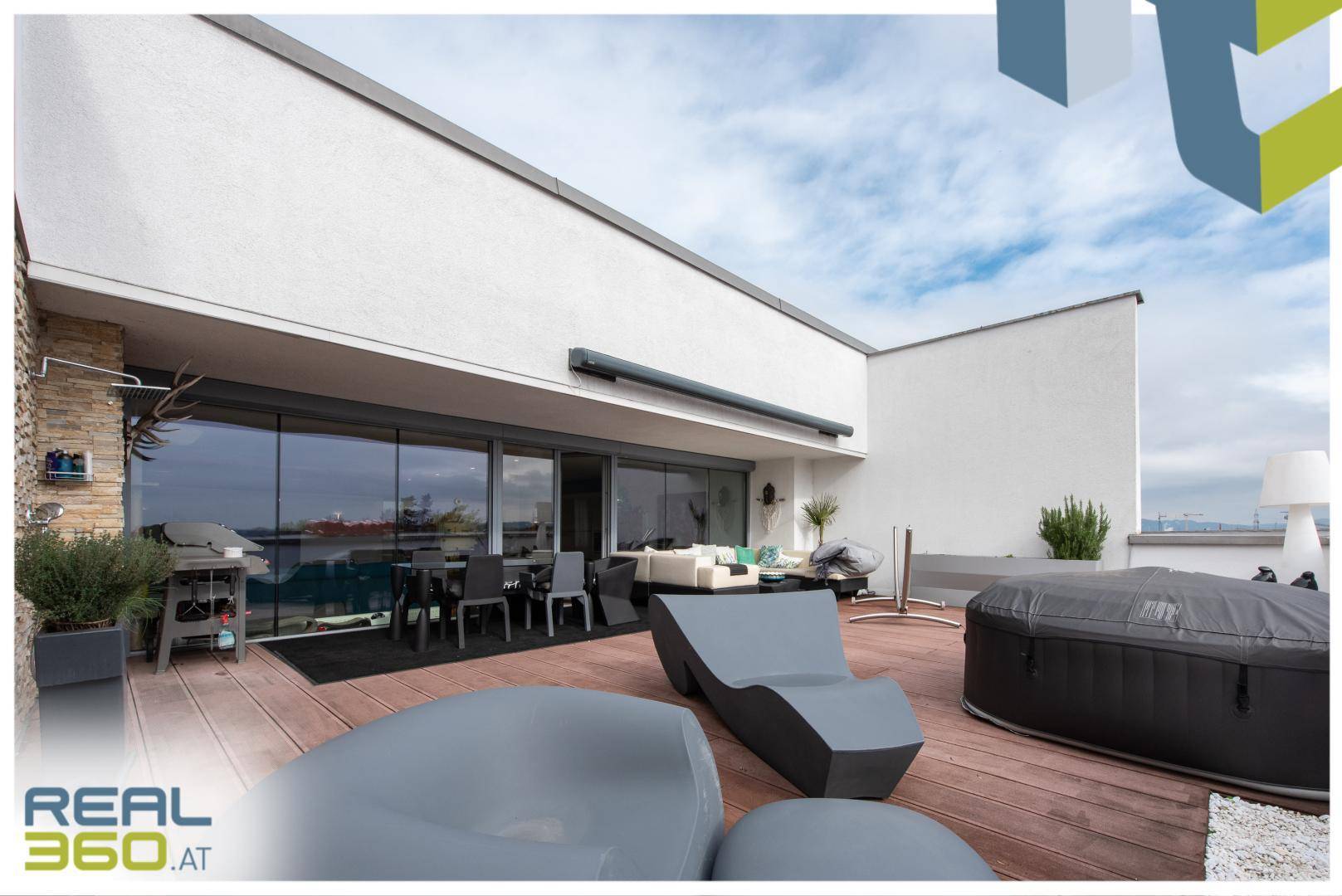Große Terrasse mit Lounge-Möbeln, Whirlpool und weitem Blick unter blauem Himmel.