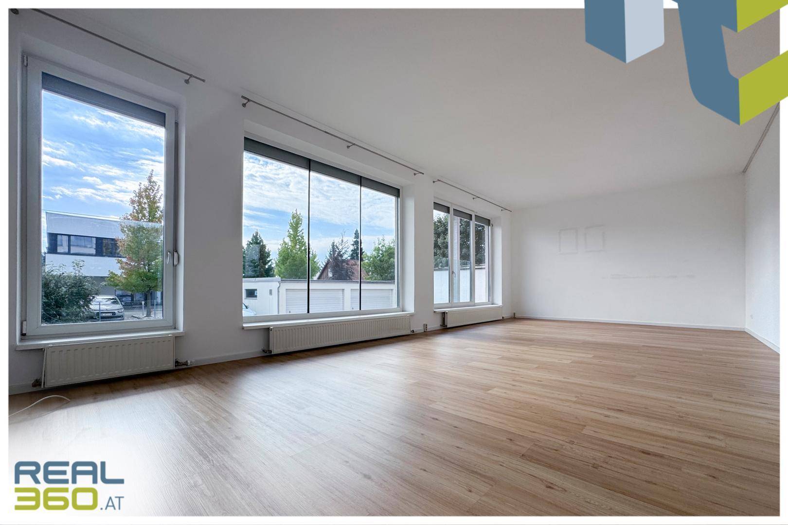 Geräumiges, helles Wohnzimmer mit großen Fenstern und neuem Laminatboden, bereit zur Einrichtung.