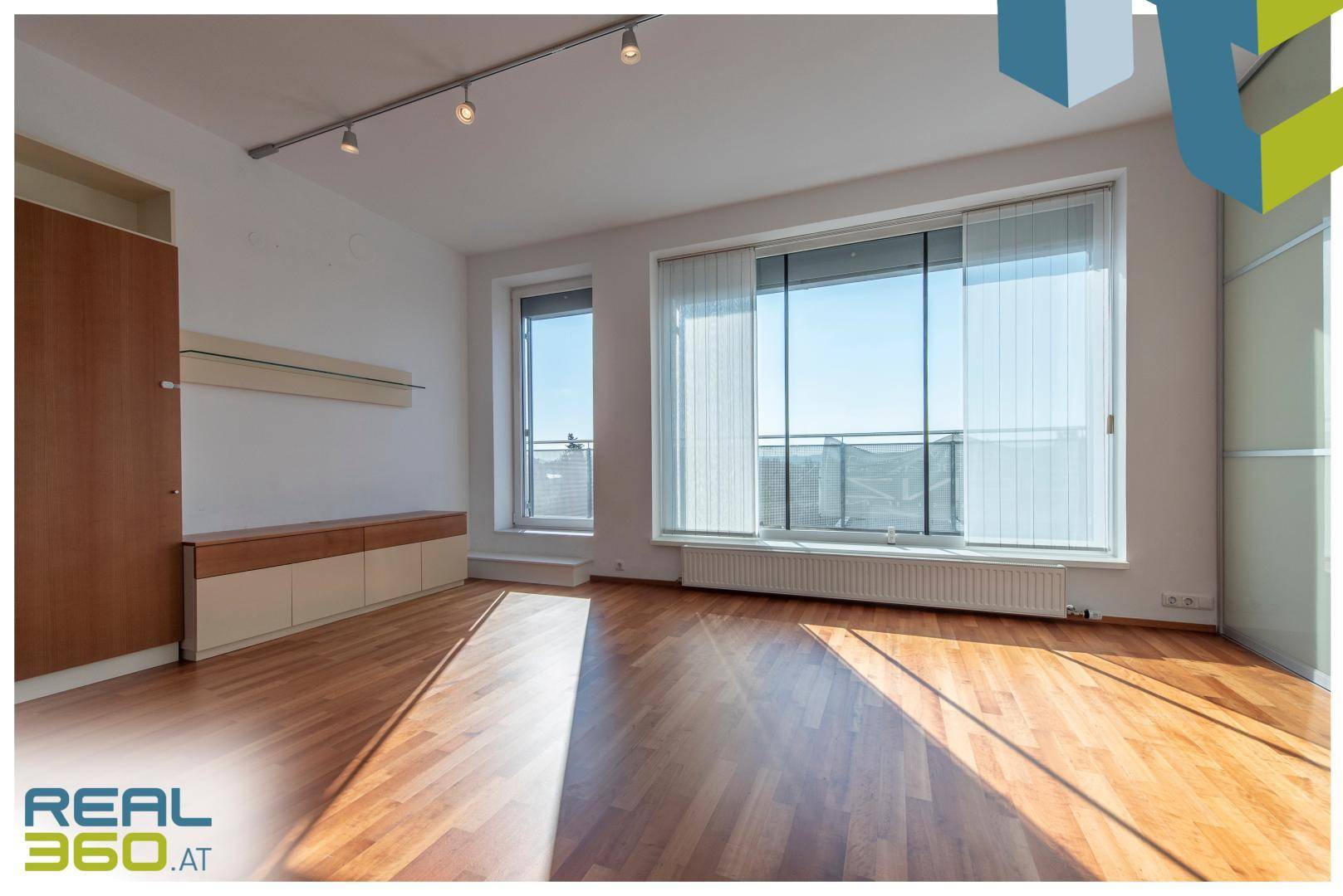 Heller Wohnbereich mit Parkettboden, großen Fenstern und direktem Zugang zum Balkon.