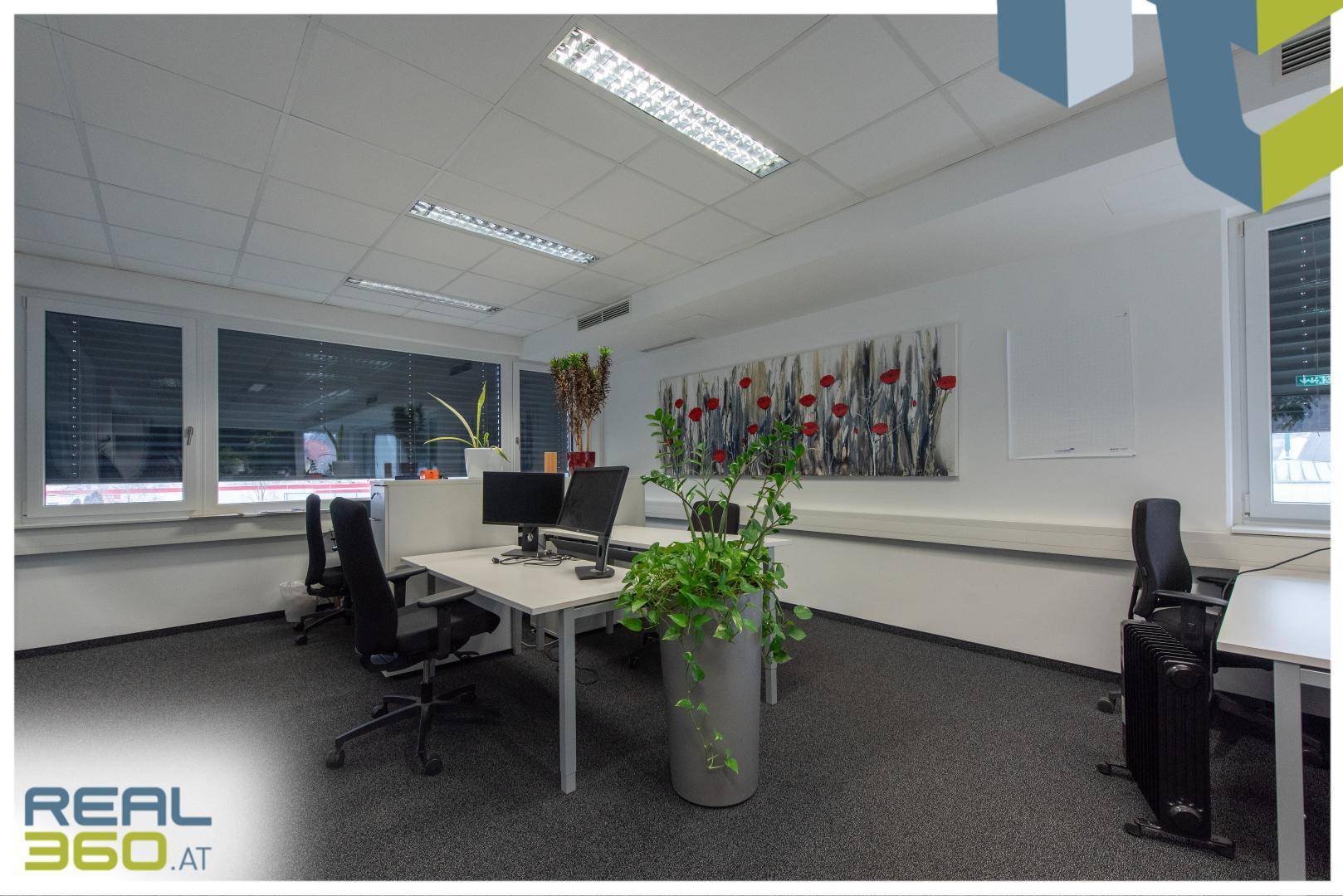 Modernes Büro mit mehreren Schreibtischen, Teppichboden und einem großen Kunstwerk an der Wand.