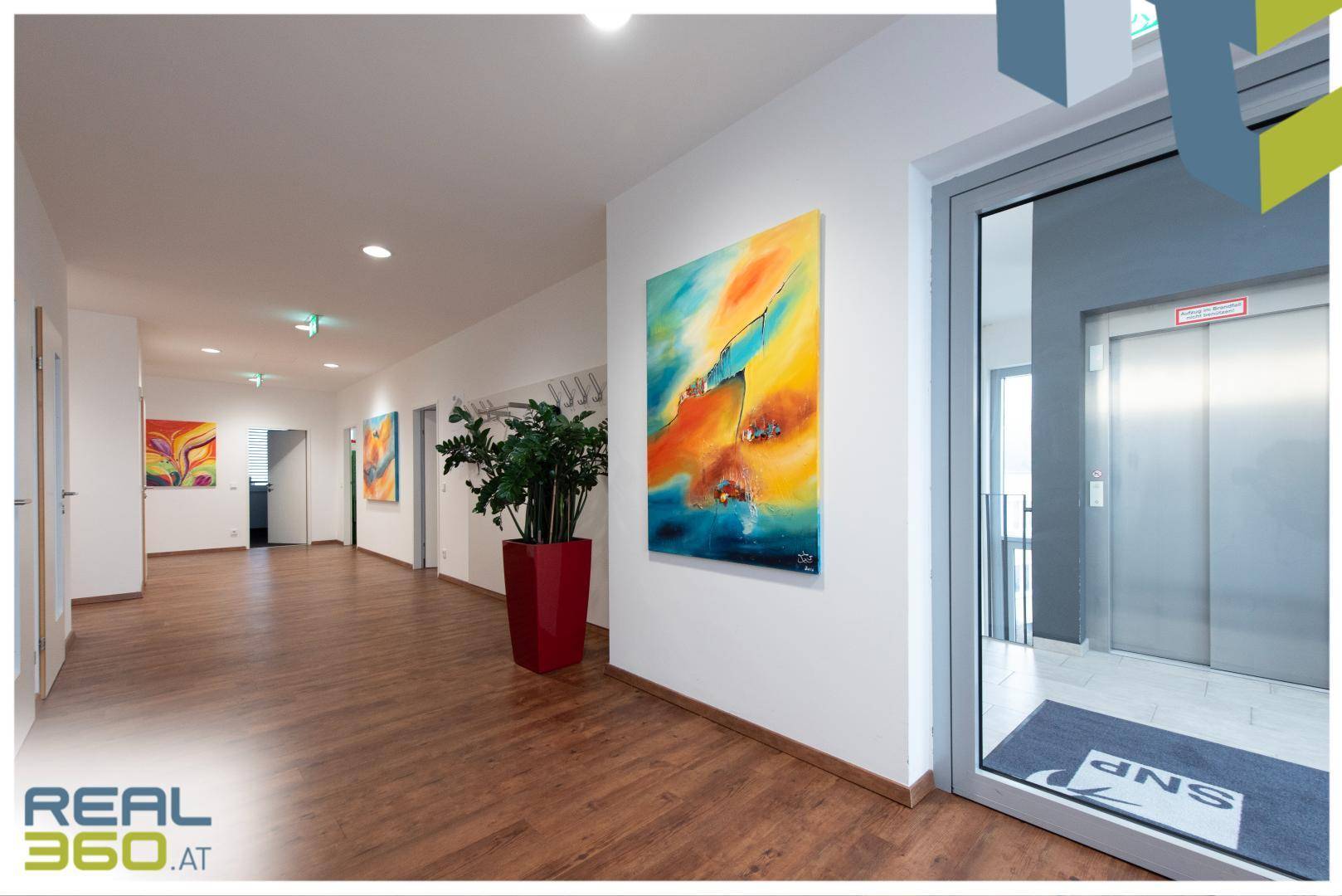 Heller Flur mit Holzboden, modernen Kunstwerken und Zugang zu einem Aufzug.