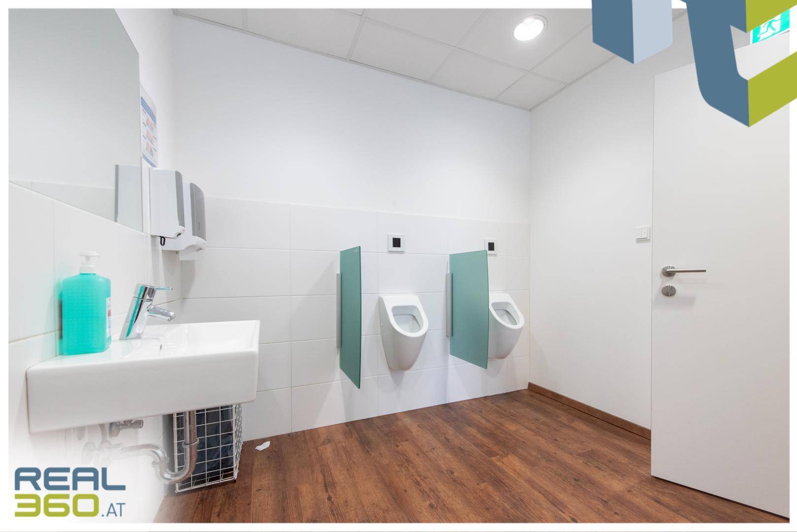 Moderner Herrenwaschraum mit zwei Urinalen, Waschbecken und Holzboden, sauber und funktional.