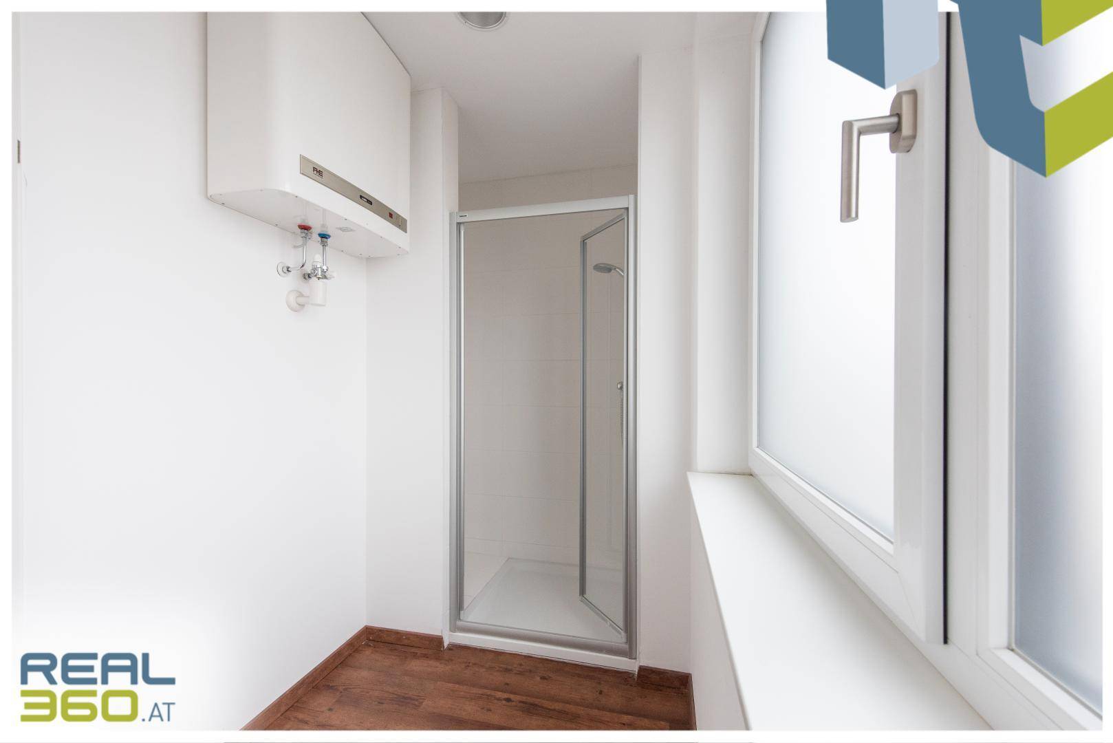 Kleines Badezimmer mit Duschkabine, Fenster und Warmwasserbereiter, funktional und hell.