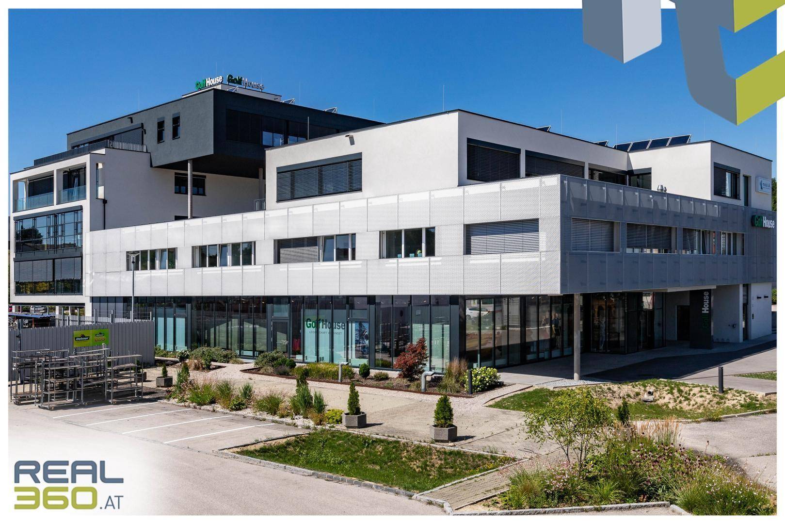 Großes modernes Geschäftsgebäude mit mehreren Etagen, Parkplätzen und gepflegter Außenanlage.