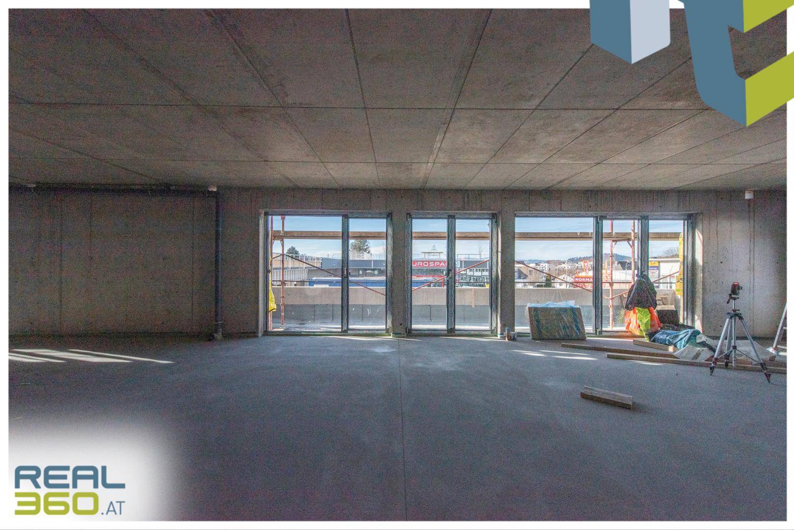 Heller Gewerberaum im Rohbau mit Betonboden und weitem Blick durch die Fenster.