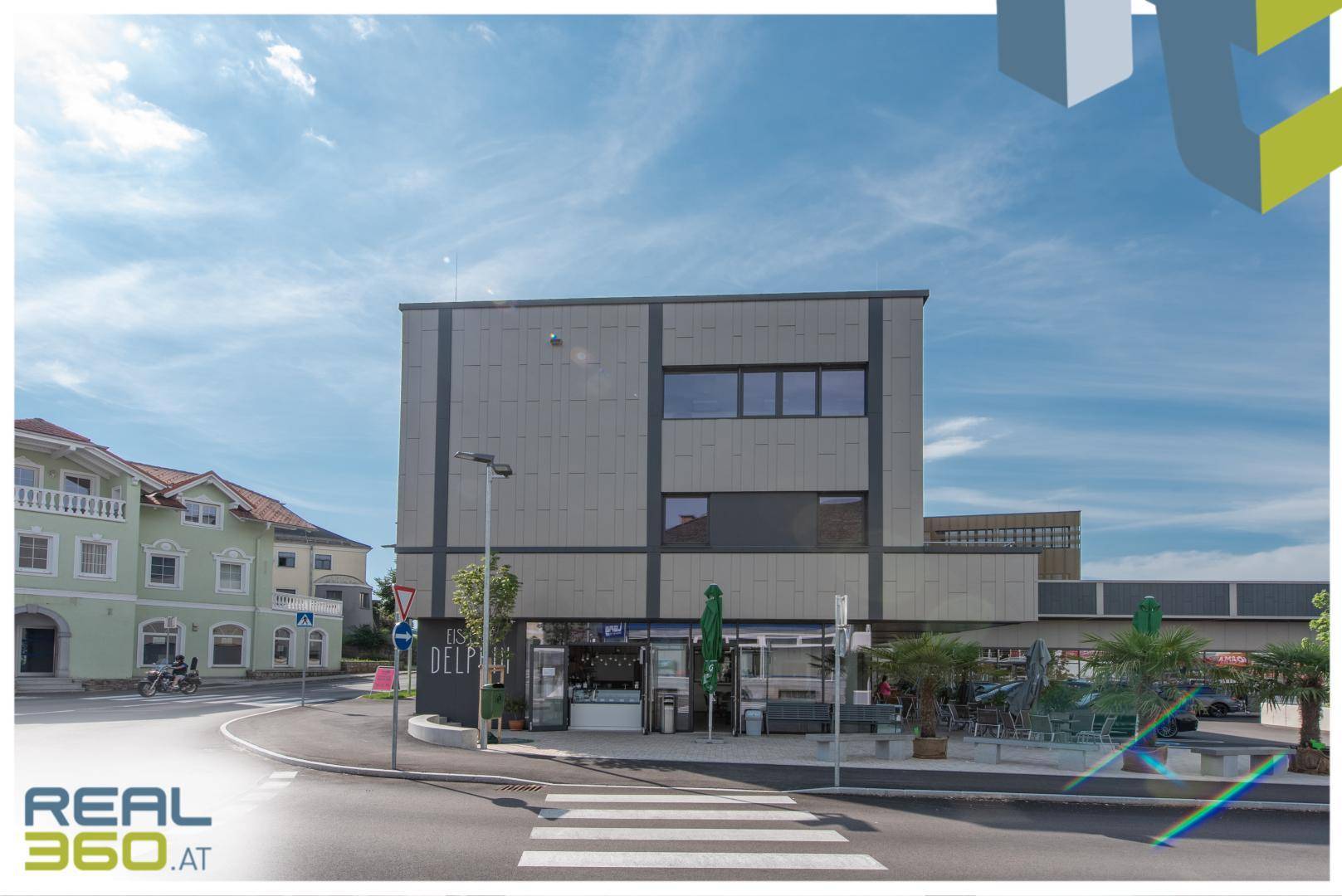 Zeitgenössisches Geschäftsgebäude an einer Straßenecke mit Fußgängerüberweg und umliegender Bebauung.