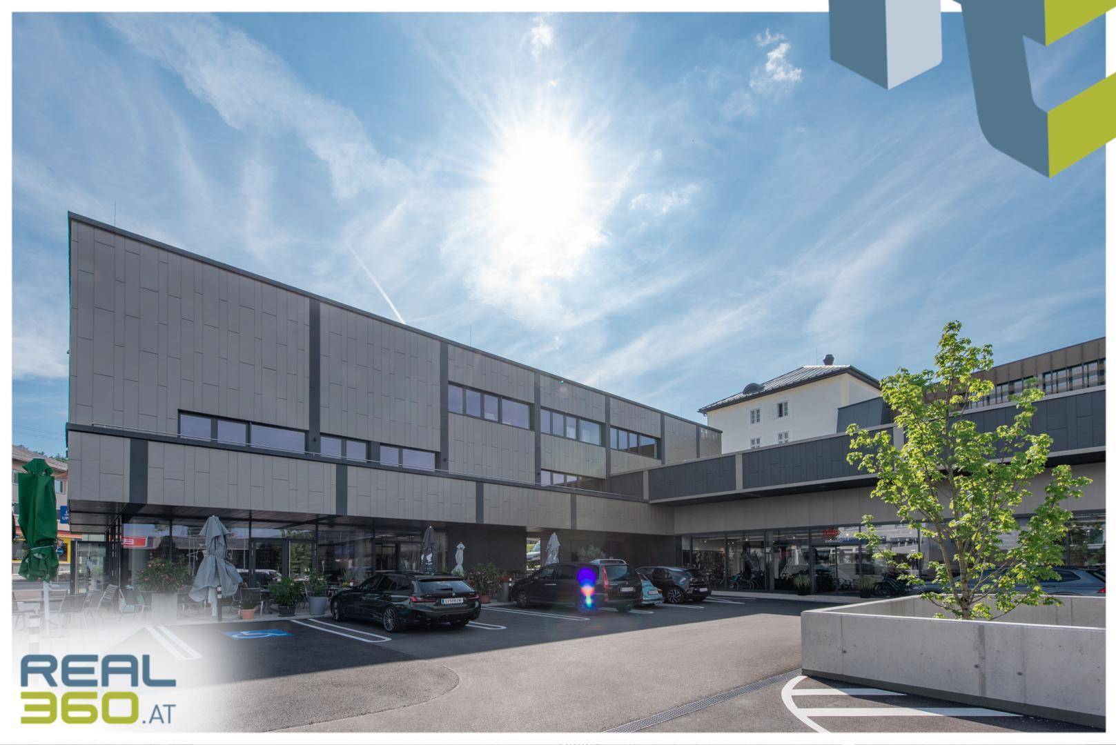 Modernes Geschäftsgebäude mit großzügigen Fensterfronten und einem Parkplatz unter strahlendem Sonnenschein.