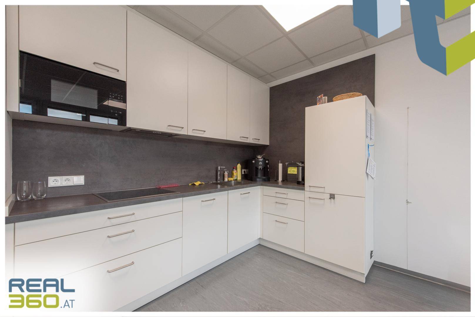 Moderne Einbauküche mit weißen Schränken, dunkler Arbeitsplatte und integrierten Geräten.