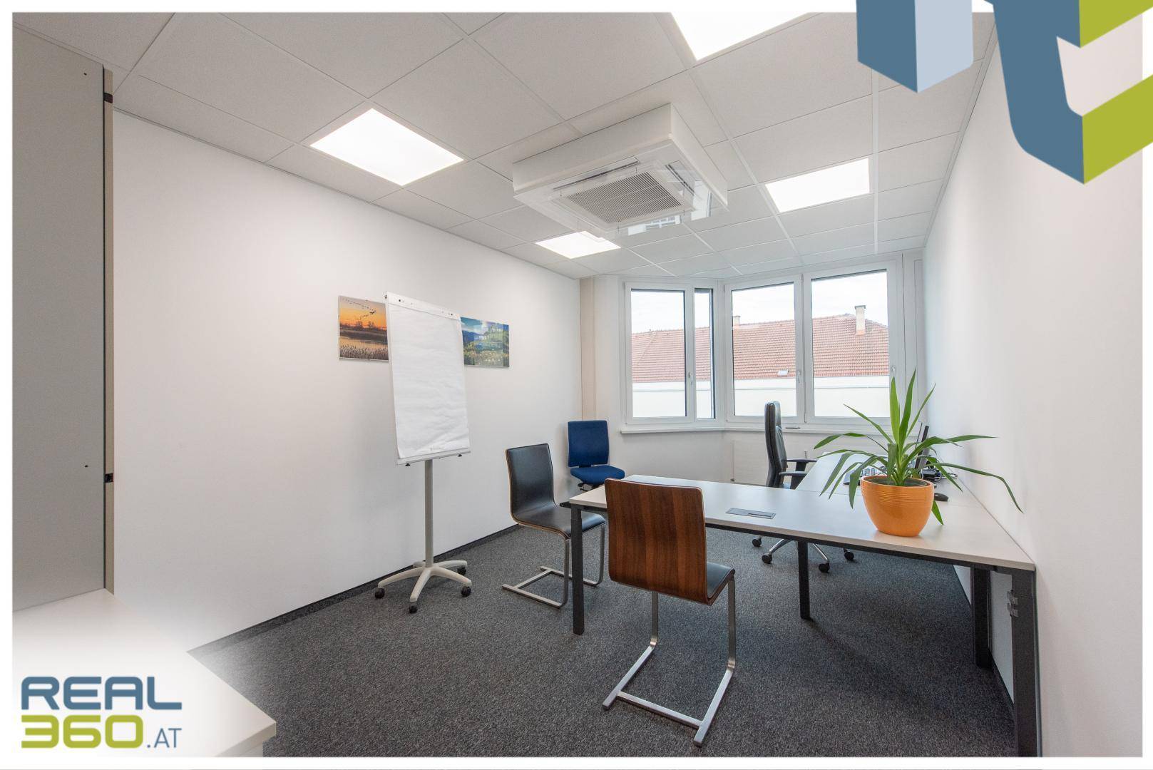 Modernes Büro mit Besprechungstisch, Flipchart, Klimaanlage und großen Fenstern.