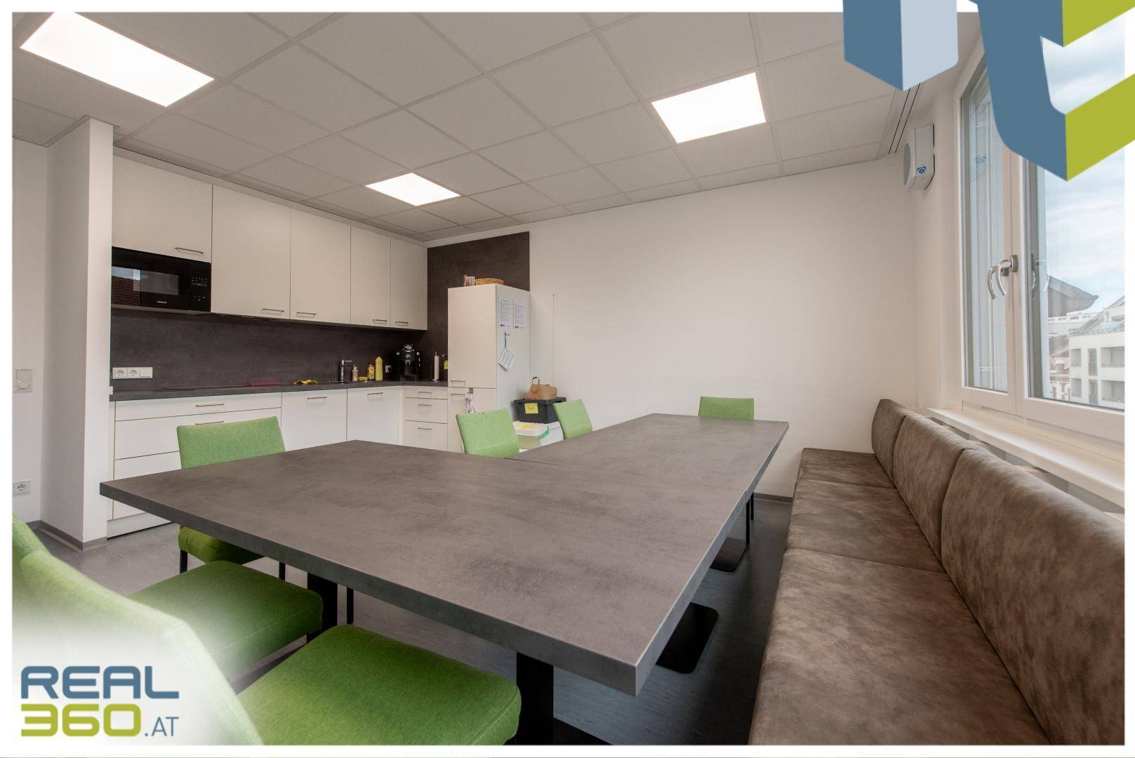 Großzügige Pausenküche mit langer Tafel, grünen Stühlen und integrierter Küchenzeile.
