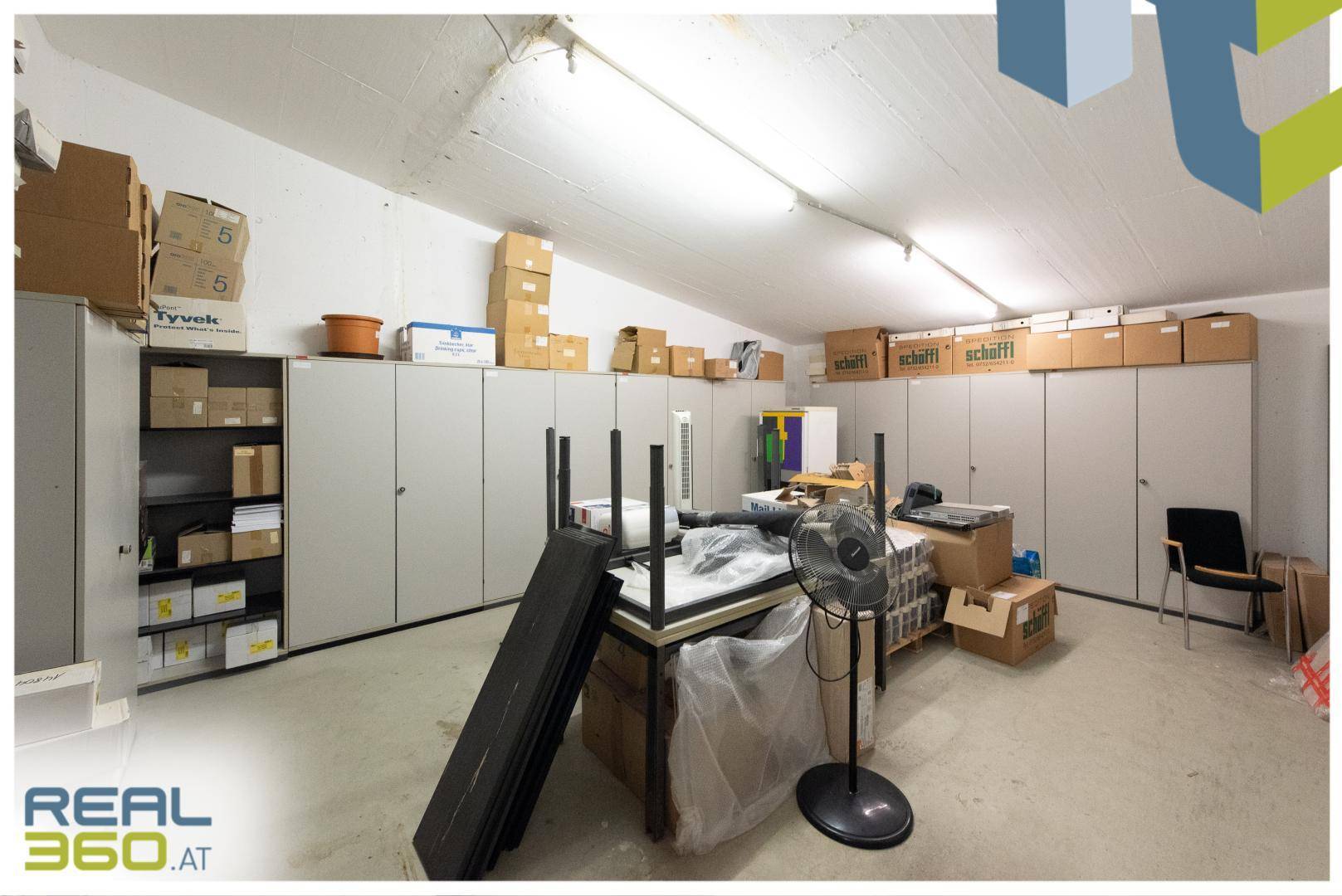 Geräumiger Lagerraum mit vielen Regalen, Kartons und einem Ventilator unter der Decke.