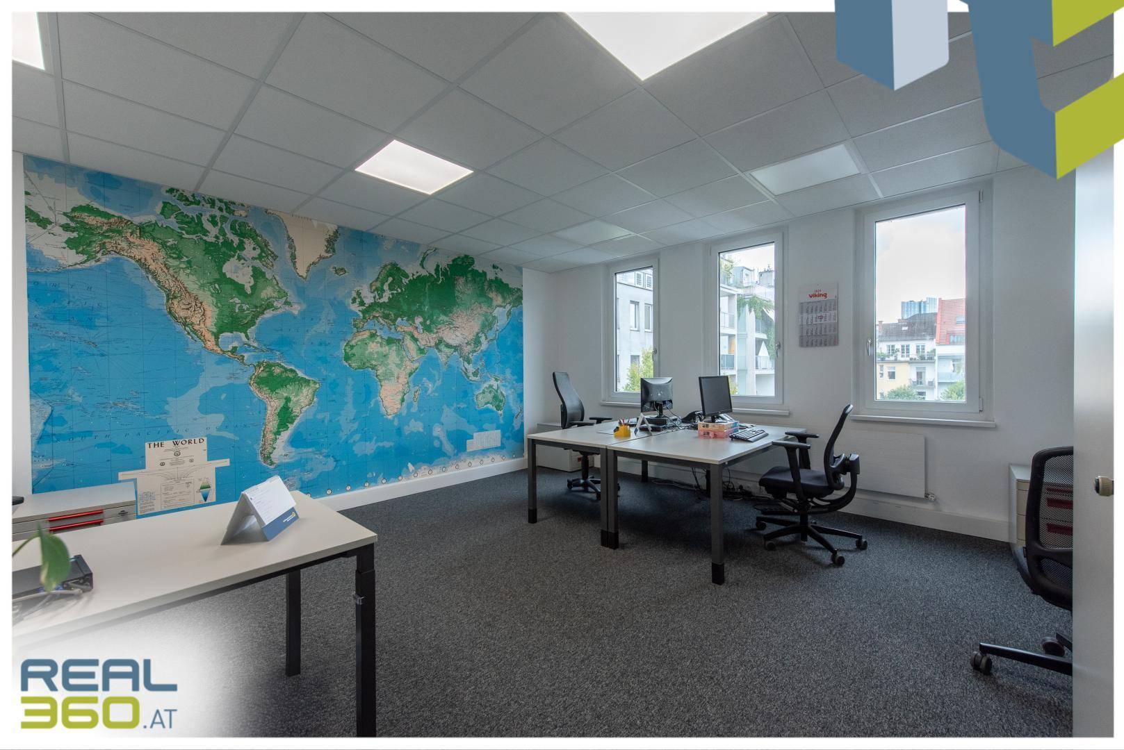 Modernes Büro mit Weltkarte an der Wand, mehreren Arbeitsplätzen und großen Fenstern mit Ausblick.
