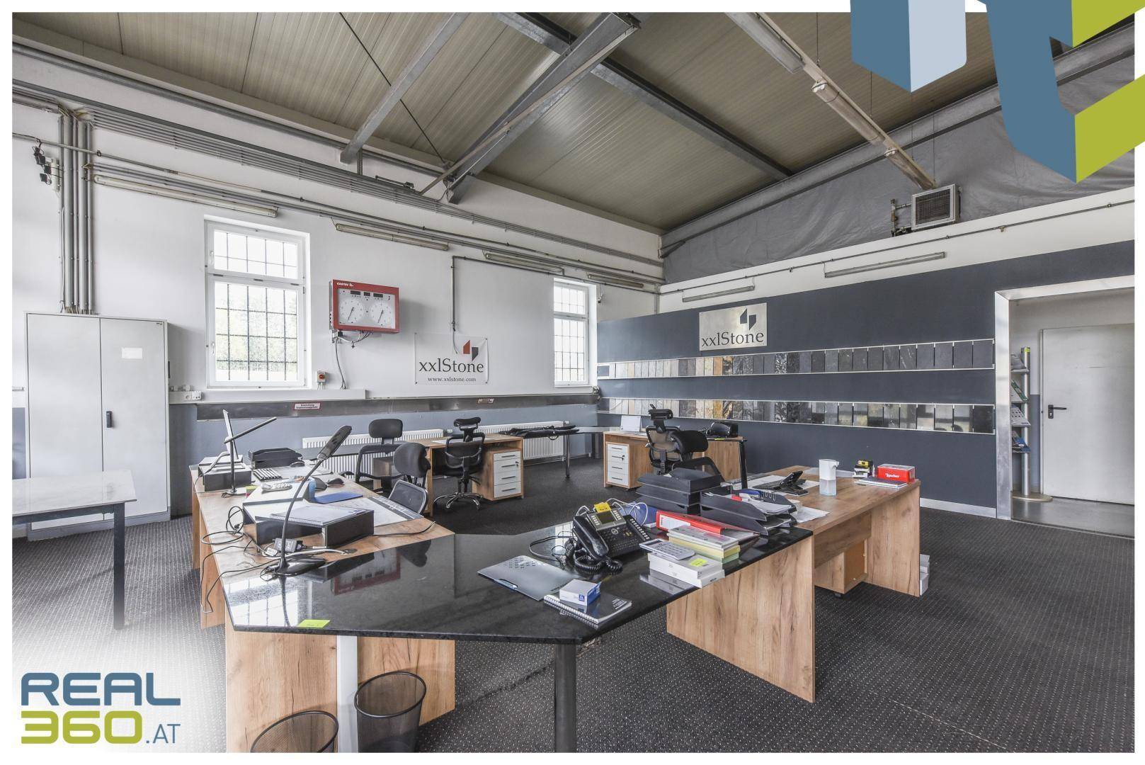 Großes offenes Büro mit mehreren Arbeitsplätzen, hohen Decken und Produktpräsentationen an der Wand.