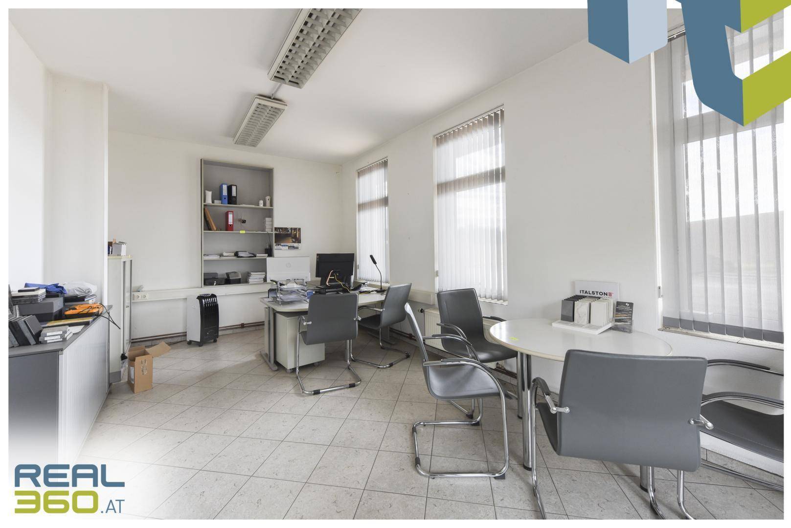 Helles Büro mit weißen Wänden, Fliesenboden, mehreren Arbeitsplätzen und großen Fenstern.