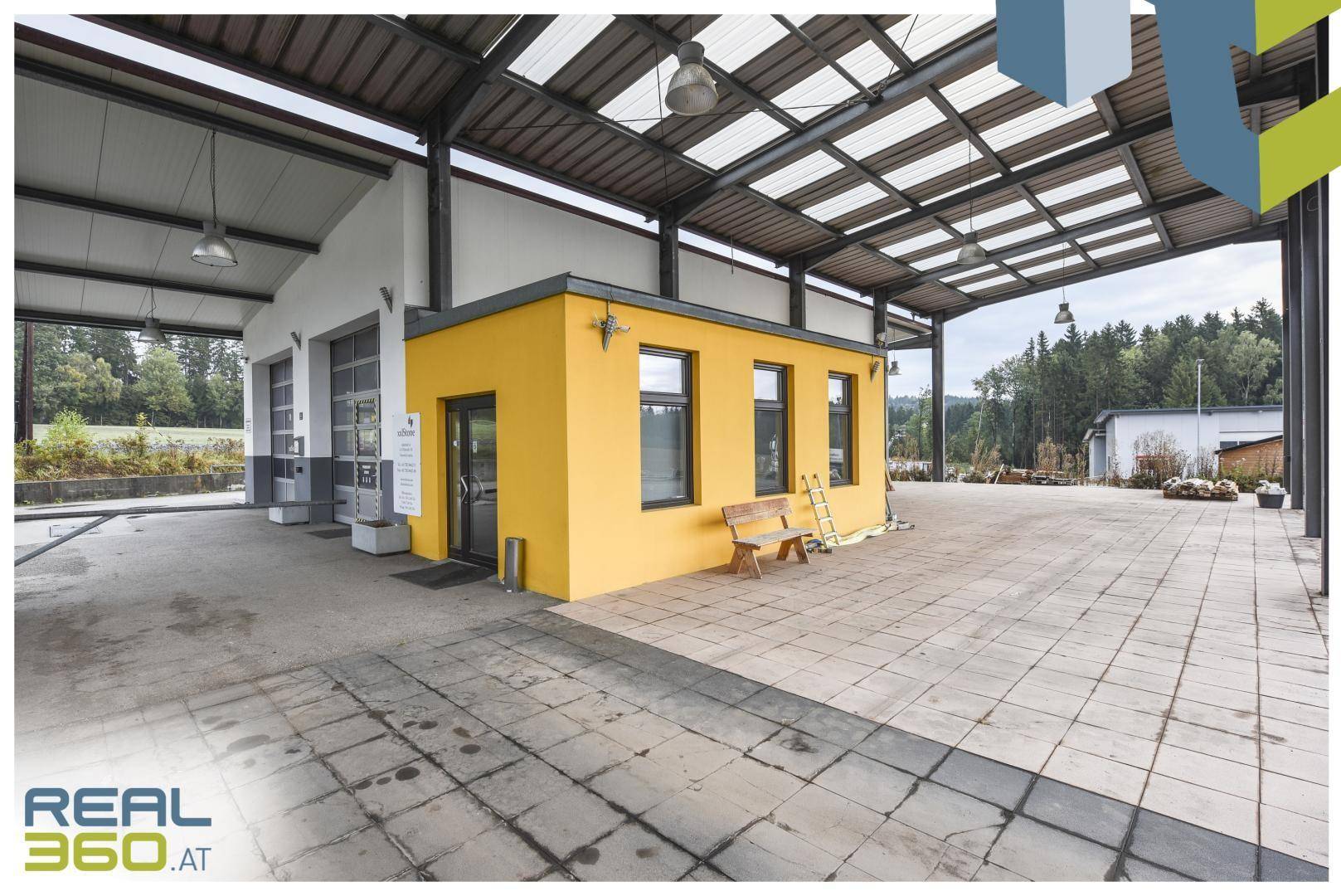 Überdachter Bereich mit gepflastertem Boden, gelbem Bürogebäude und Blick auf die Umgebung.