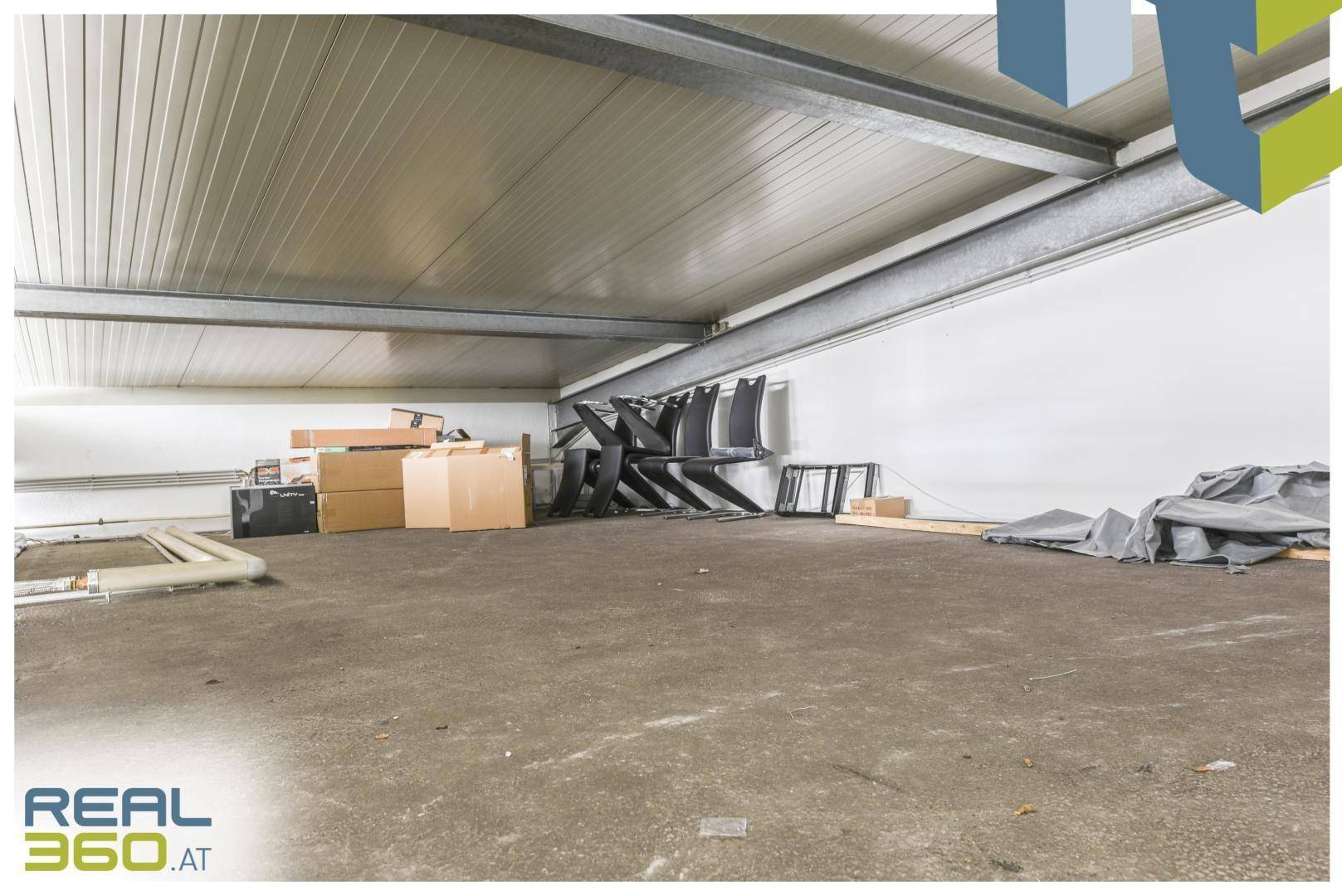 Großer leerer Lagerraum mit Betonboden, hohen Decken und einigen gelagerten Gegenständen.