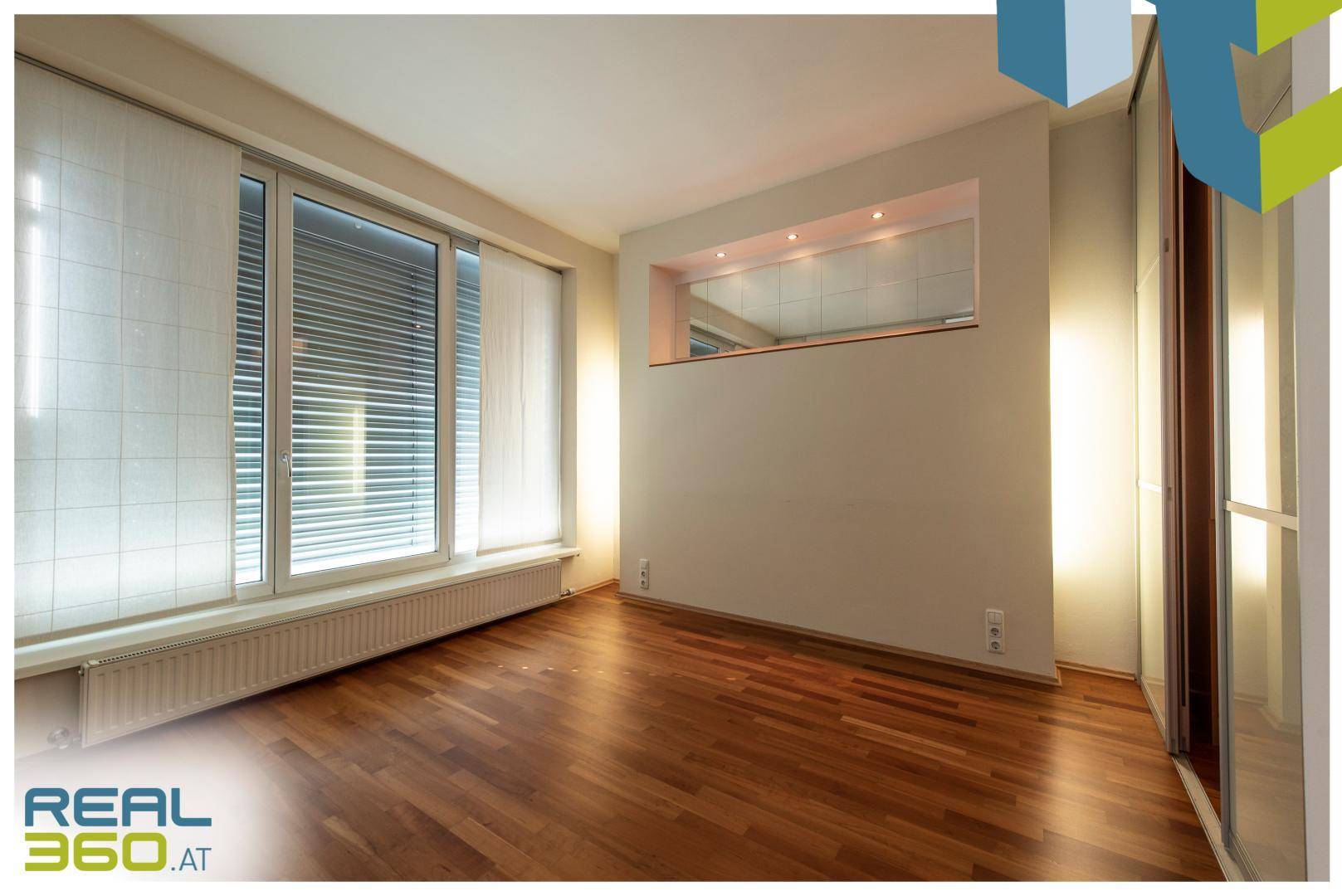 Schlafzimmer mit Parkettboden, großen Fenstern und integrierten Schränken, beleuchtet.