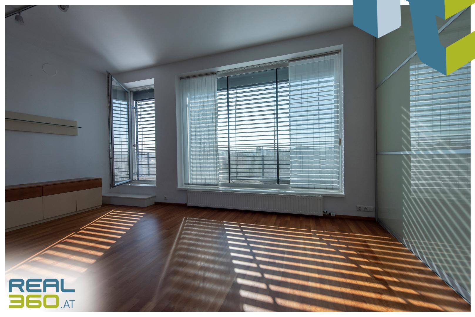 Lichtdurchfluteter Raum mit Parkettboden und großen Fenstern, die viel Sonnenlicht hereinlassen.