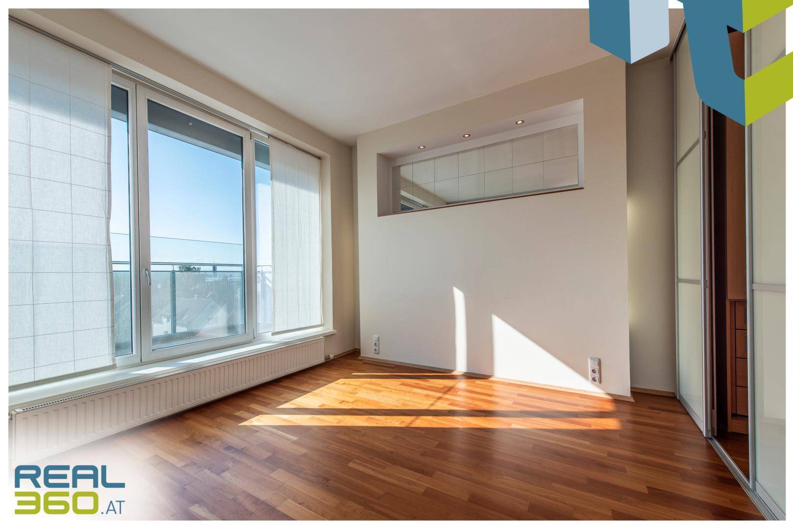 Schlafzimmer mit Parkettboden, großen Fenstern und integrierten Schränken.