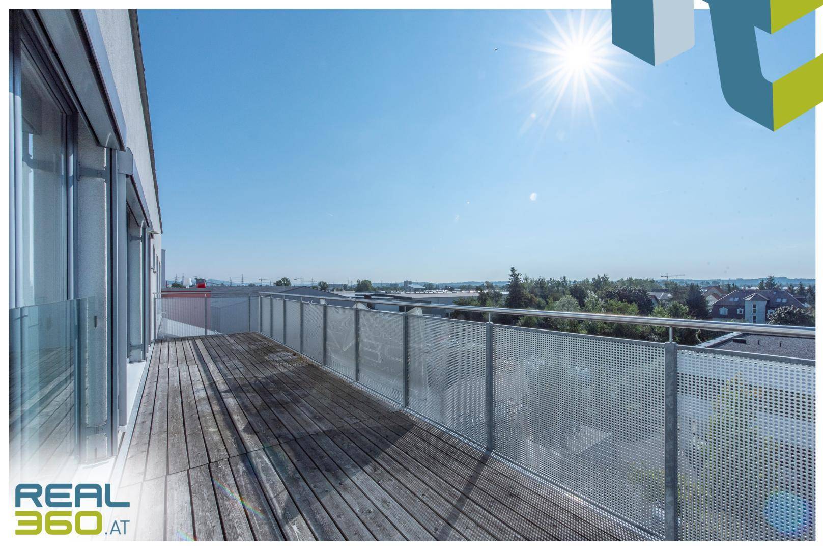 Große sonnige Terrasse mit Holzboden und Metallgeländer, bietet weite Aussicht.