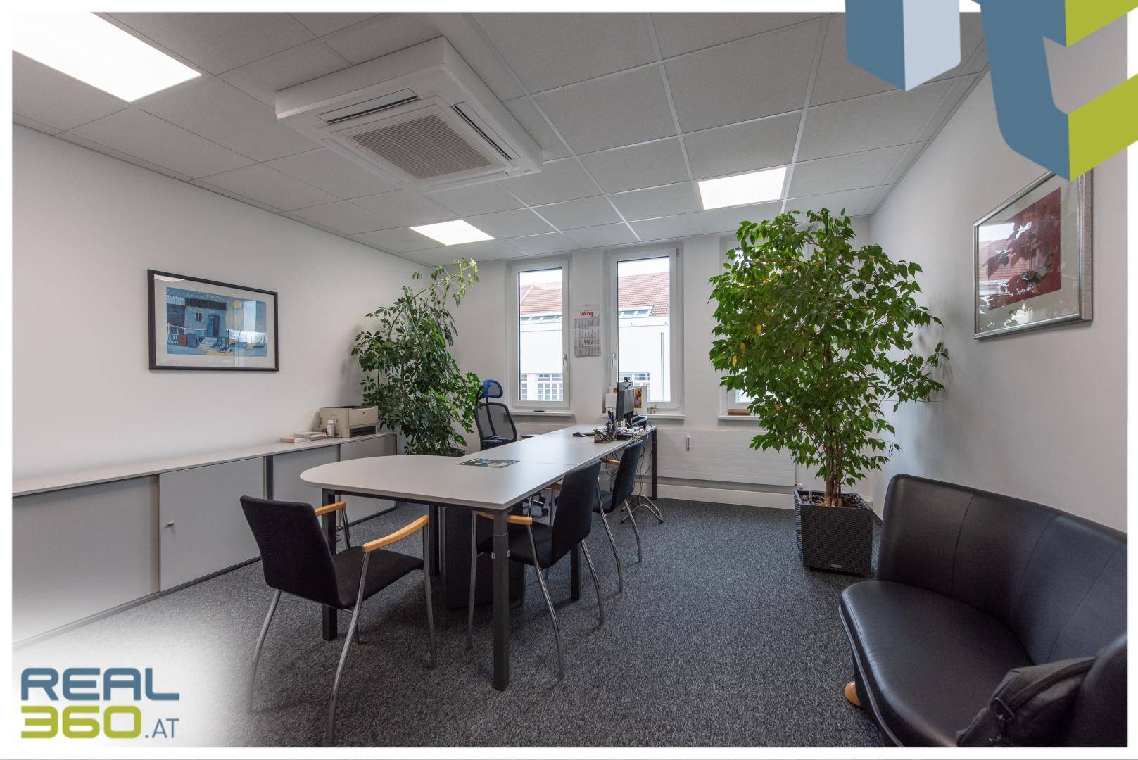 Geräumiges Büro mit mehreren Arbeitsplätzen, grünen Pflanzen und Blick auf die Umgebung durch große Fenster.