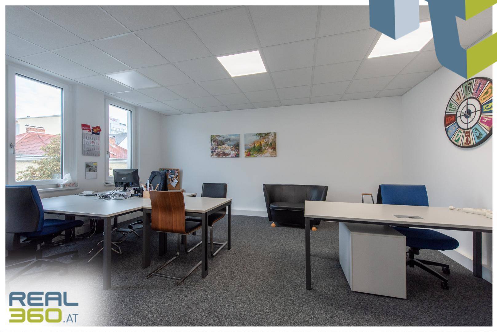 Modern eingerichtetes Büro mit mehreren Arbeitsplätzen, einem Sofa und farbenfroher Wanddekoration.