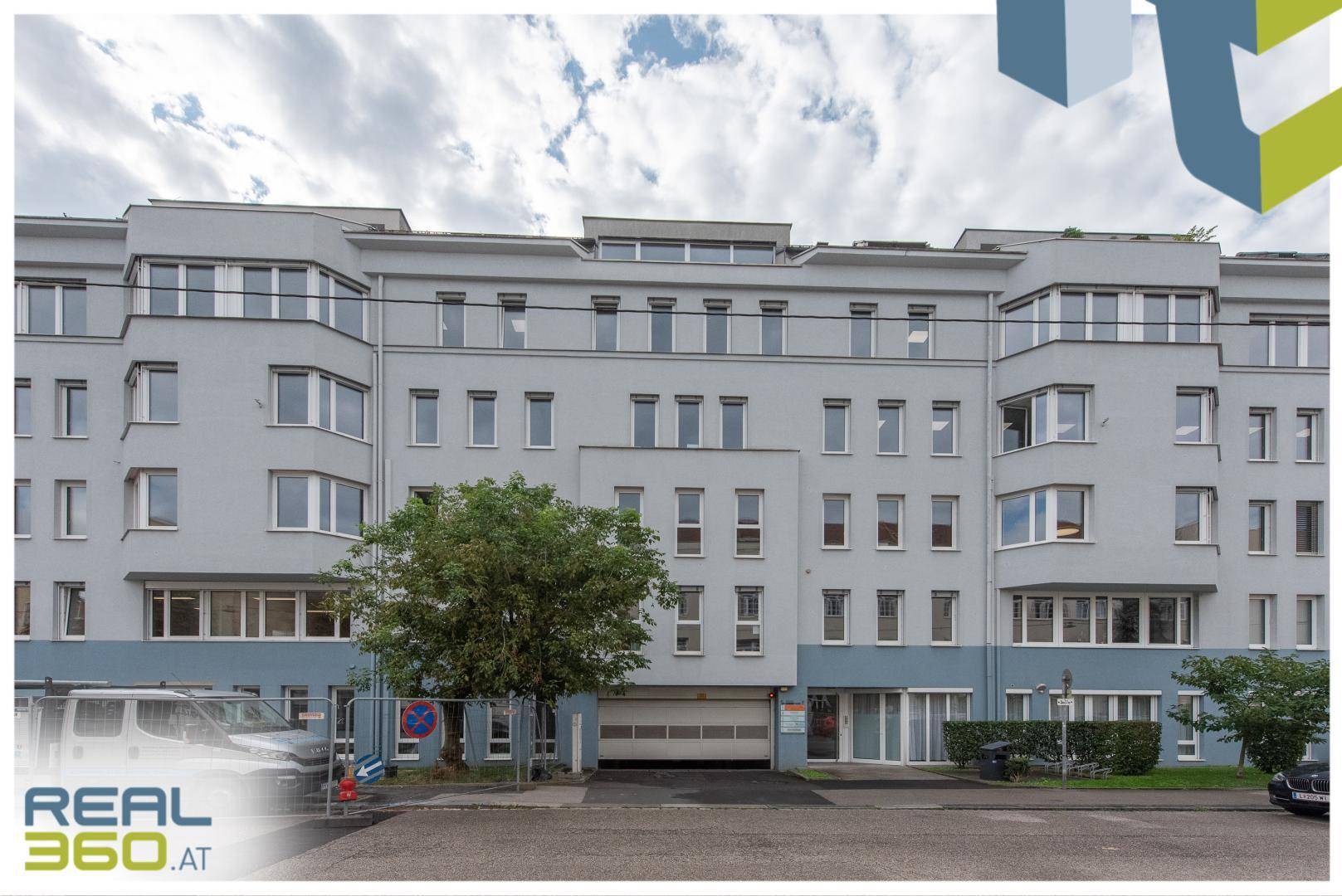 Ansicht eines modernen Bürogebäudes mit vielen Fenstern und einer Tiefgarageneinfahrt.