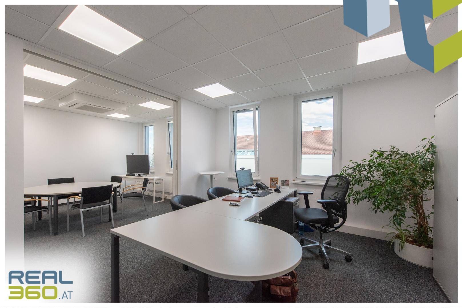 Büro mit Schreibtisch, Bürostuhl und Zugang zu einem Besprechungsraum durch eine Glastrennwand.